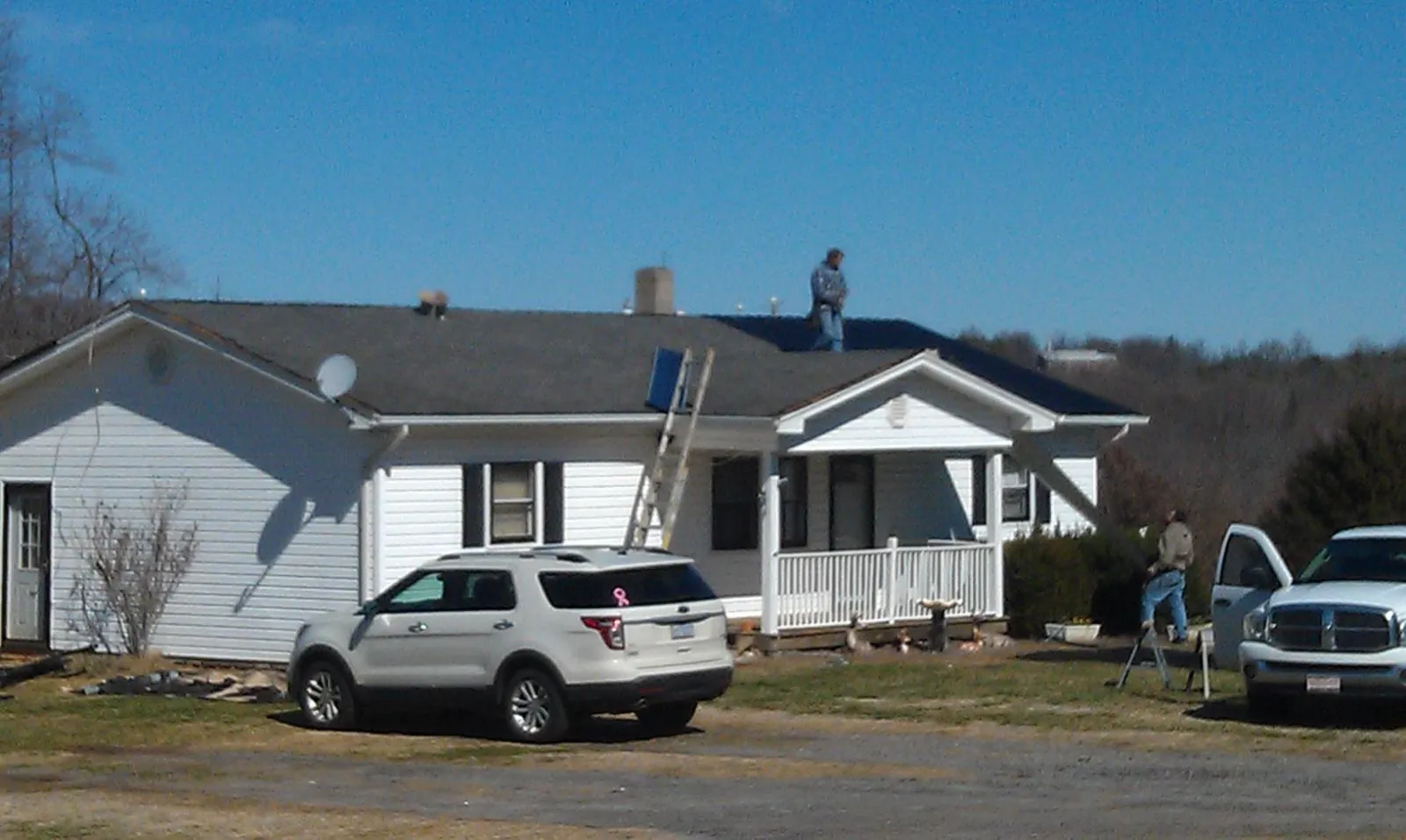 Roofers stripping shingles from a white ranch house roof in Spencer
